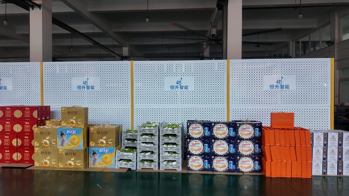 Mid-Autumn welfare gifts lined up along the HenSing production floor: autumn moon pear cartons, red nut gift boxes, green grapes in crates, Danisa butter cookies, orange pastry boxes and yogurt drink cartons